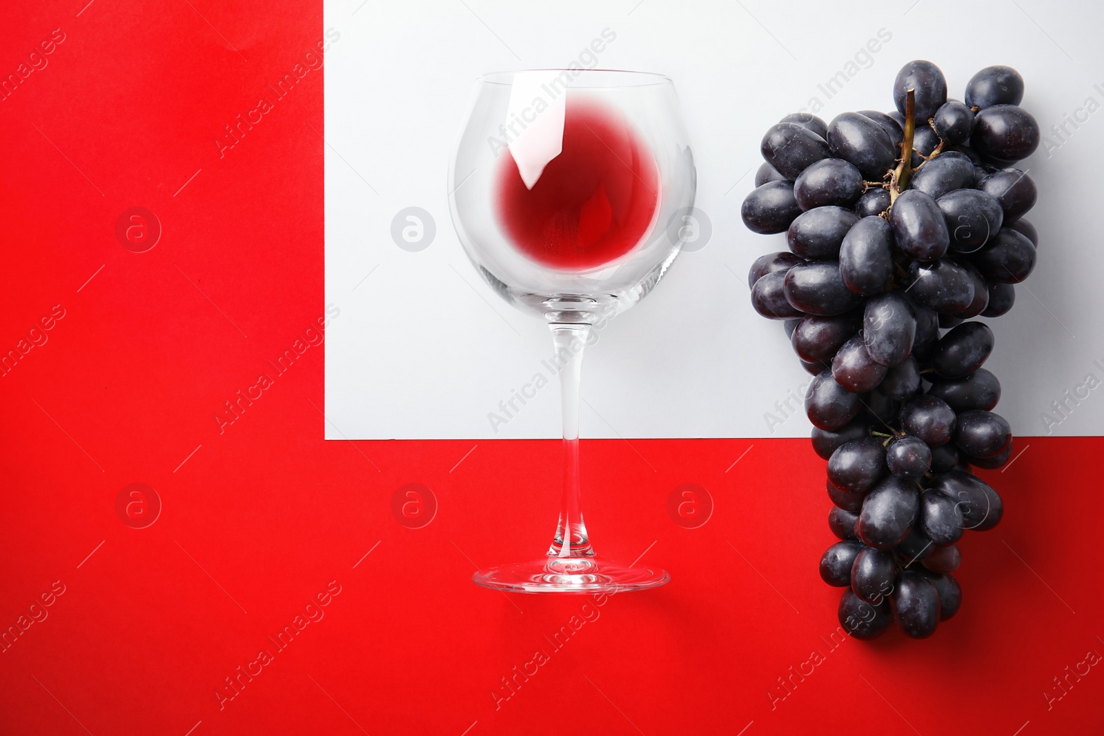Photo of Fresh ripe juicy grapes, glass with red wine and space for text on color background, top view