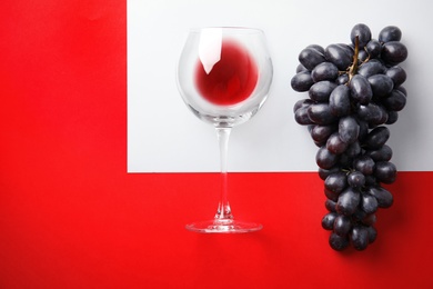 Photo of Fresh ripe juicy grapes, glass with red wine and space for text on color background, top view