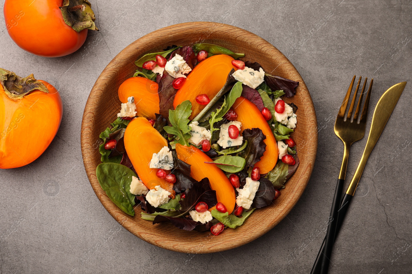 Photo of Delicious persimmon salad with cheese and pomegranate served on grey table, flat lay