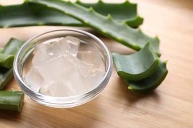 Photo of Aloe vera gel and slices of plant on wooden table, closeup