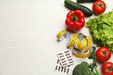 Photo of Weight loss pills, different vegetables and measuring tape on white wooden table, flat lay. Space for text