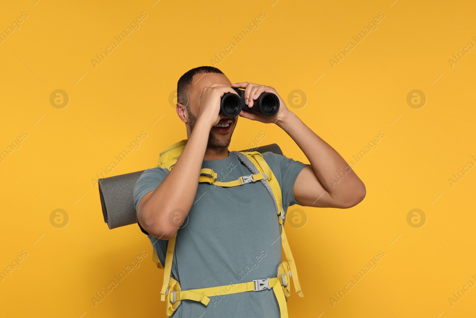 Photo of Happy tourist with backpack looking through binoculars on yellow background