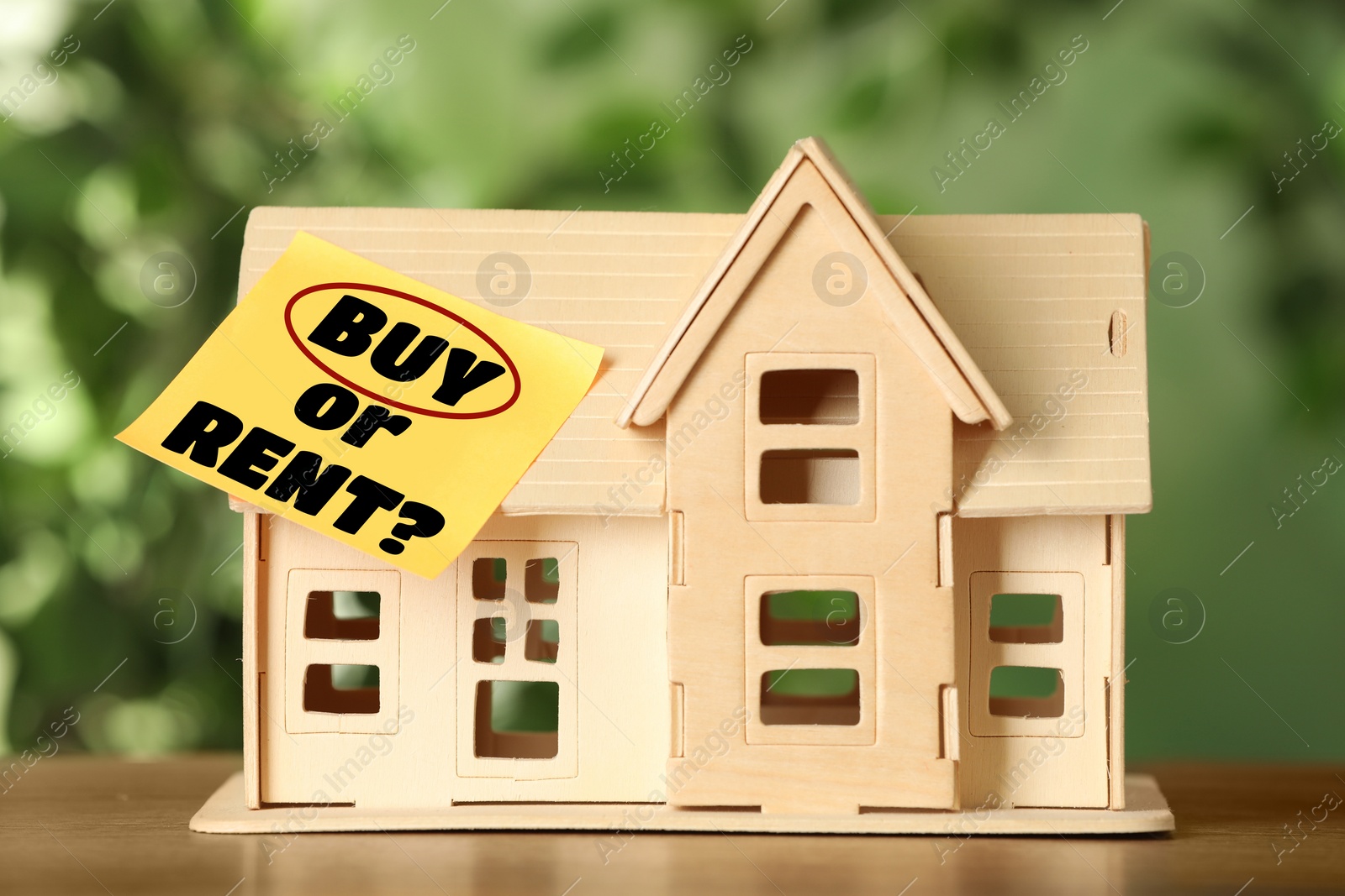 Image of Model of house with sticky note Buy Or Rent on wooden table against blurred green background