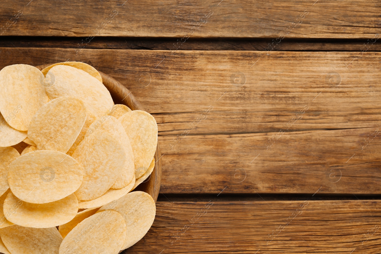 Photo of Bowl with delicious potato chips on wooden table, top view. Space for text