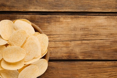 Bowl with delicious potato chips on wooden table, top view. Space for text