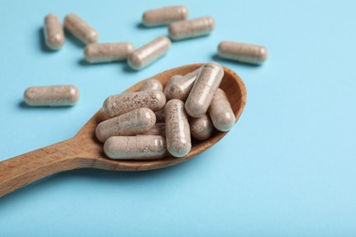 Photo of Gelatin capsules in spoon on light blue background
