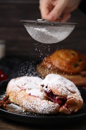 Woman dusting delicious buns with sugar powder at table, closeup