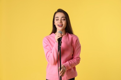 Young woman wearing casual clothes singing in microphone on color background