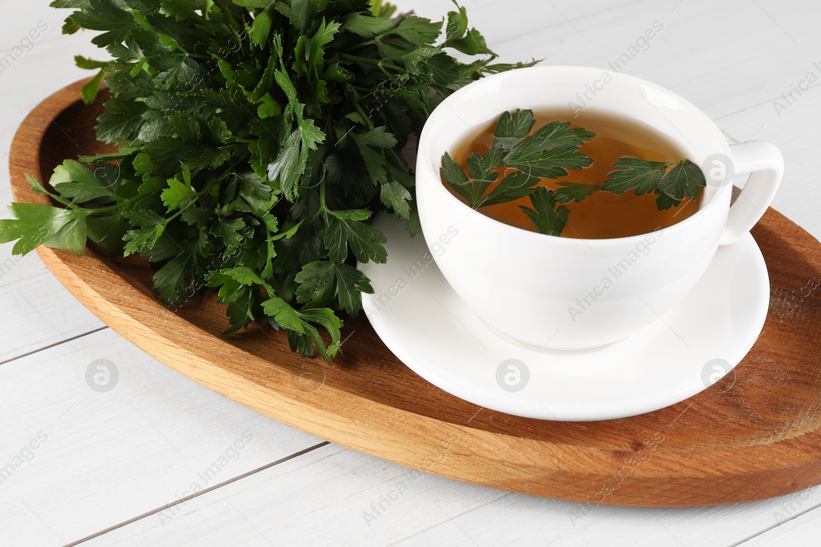 Photo of Aromatic herbal tea and fresh parsley on white wooden table