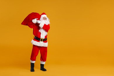 Photo of Santa Claus with bag of Christmas presents posing on orange background, space for text