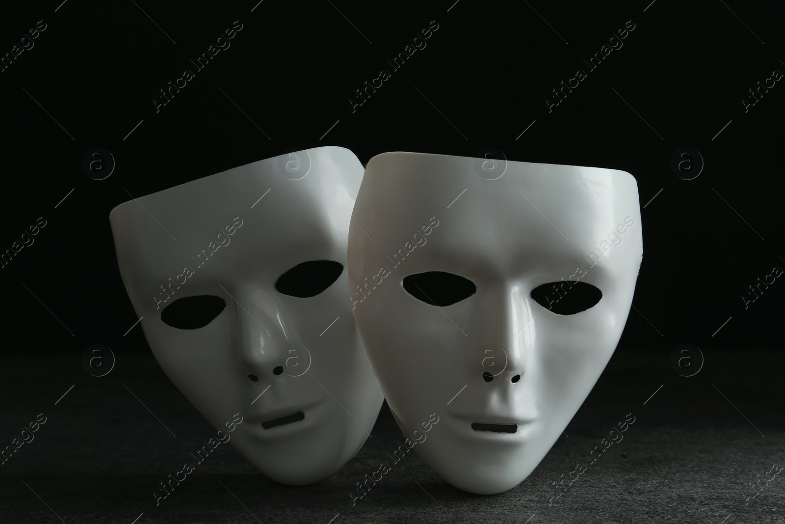 Photo of White theatre masks on grey table against black background