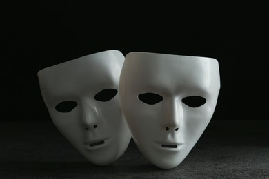 Photo of White theatre masks on grey table against black background