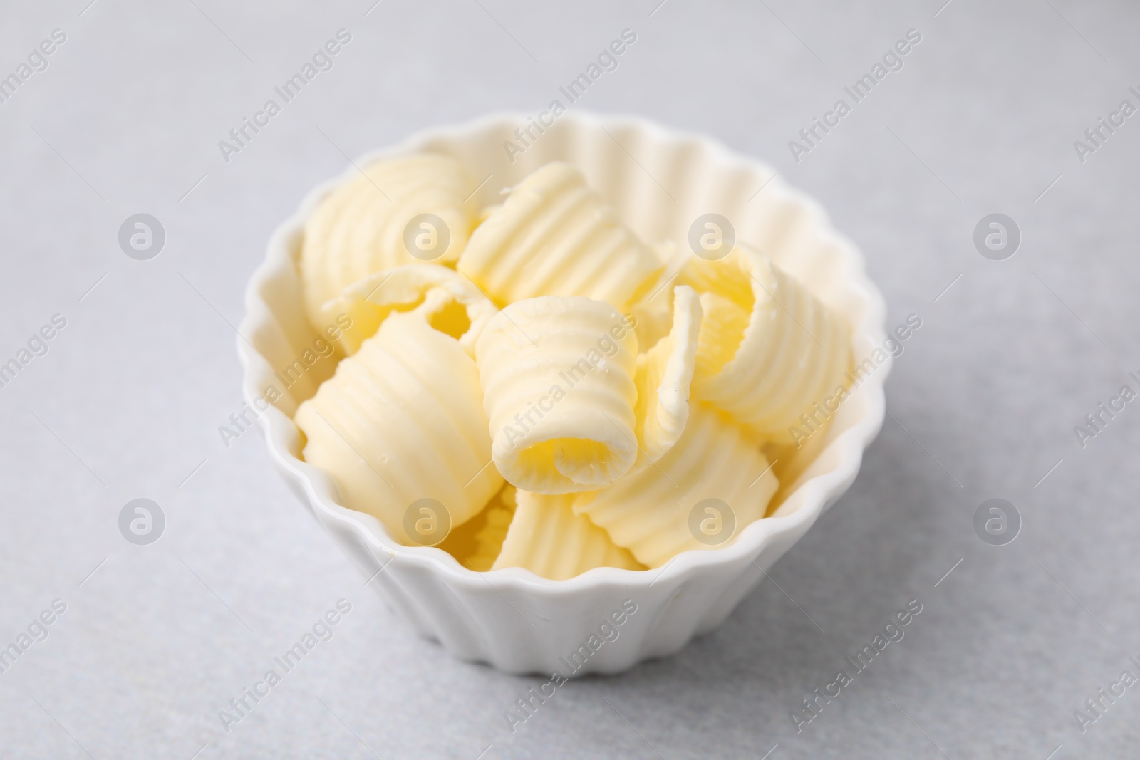 Photo of Tasty butter curls in bowl on light grey table, closeup