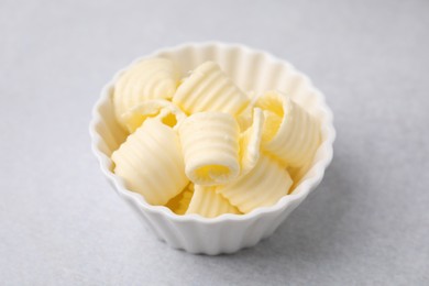 Photo of Tasty butter curls in bowl on light grey table, closeup