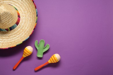 Mexican sombrero hat, maracas and toy cactus on violet background, flat lay. Space for text