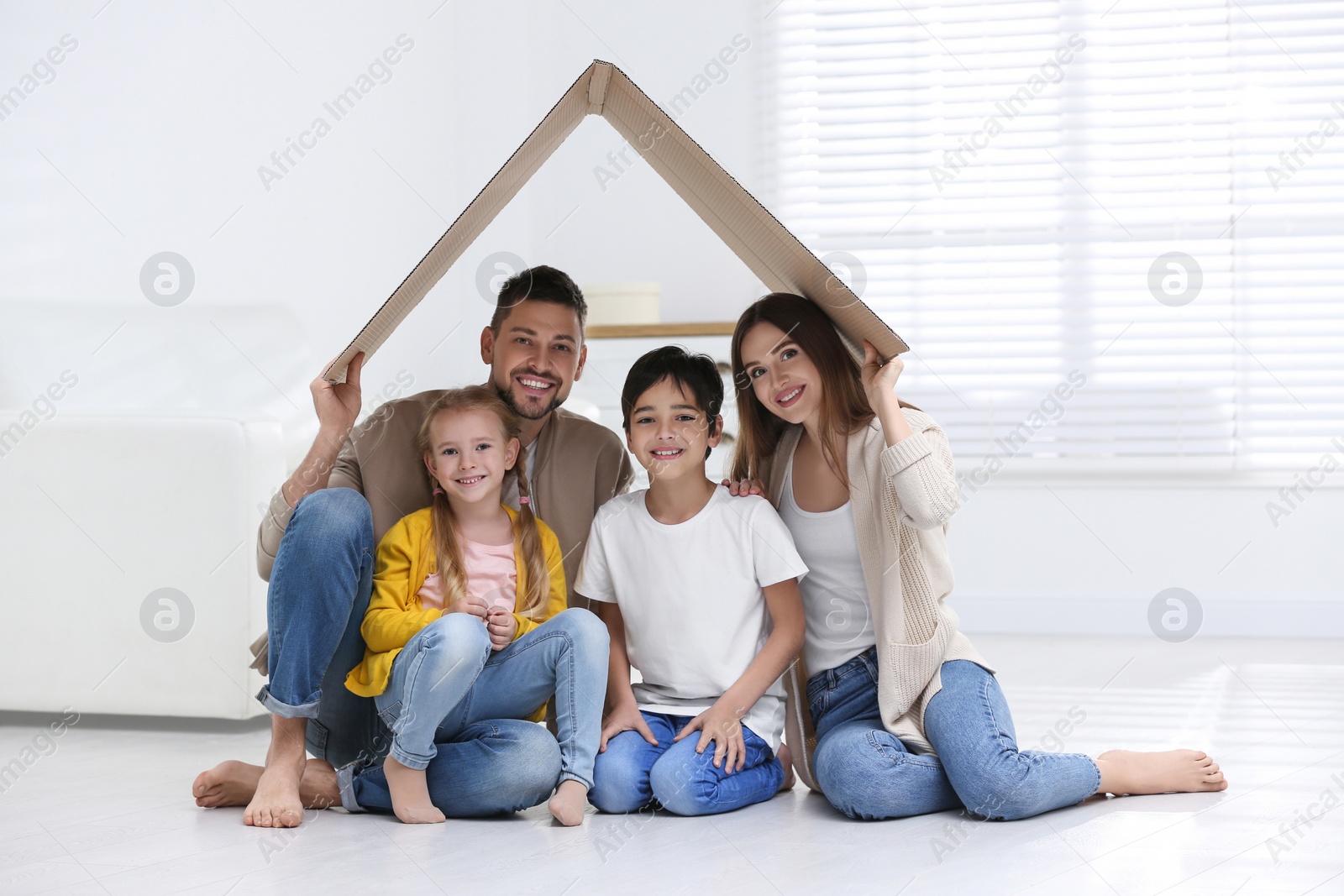 Photo of Happy family sitting under cardboard roof at home. Insurance concept