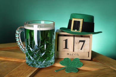 Photo of St. Patrick's day celebrating on March 17. Green beer, block calendar, leprechaun hat and decorative clover leaf on wooden table