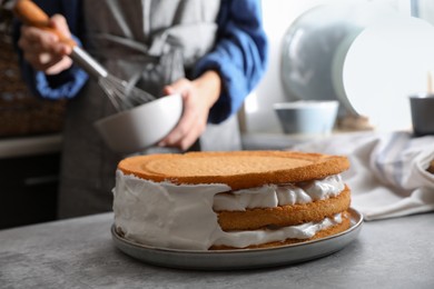 Photo of Woman decorating delicious homemade layer cake with cream at grey table, closeup