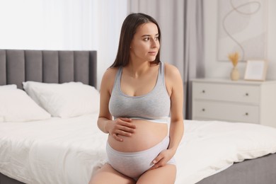 Photo of Beautiful pregnant woman in comfortable maternity underwear on bed at home