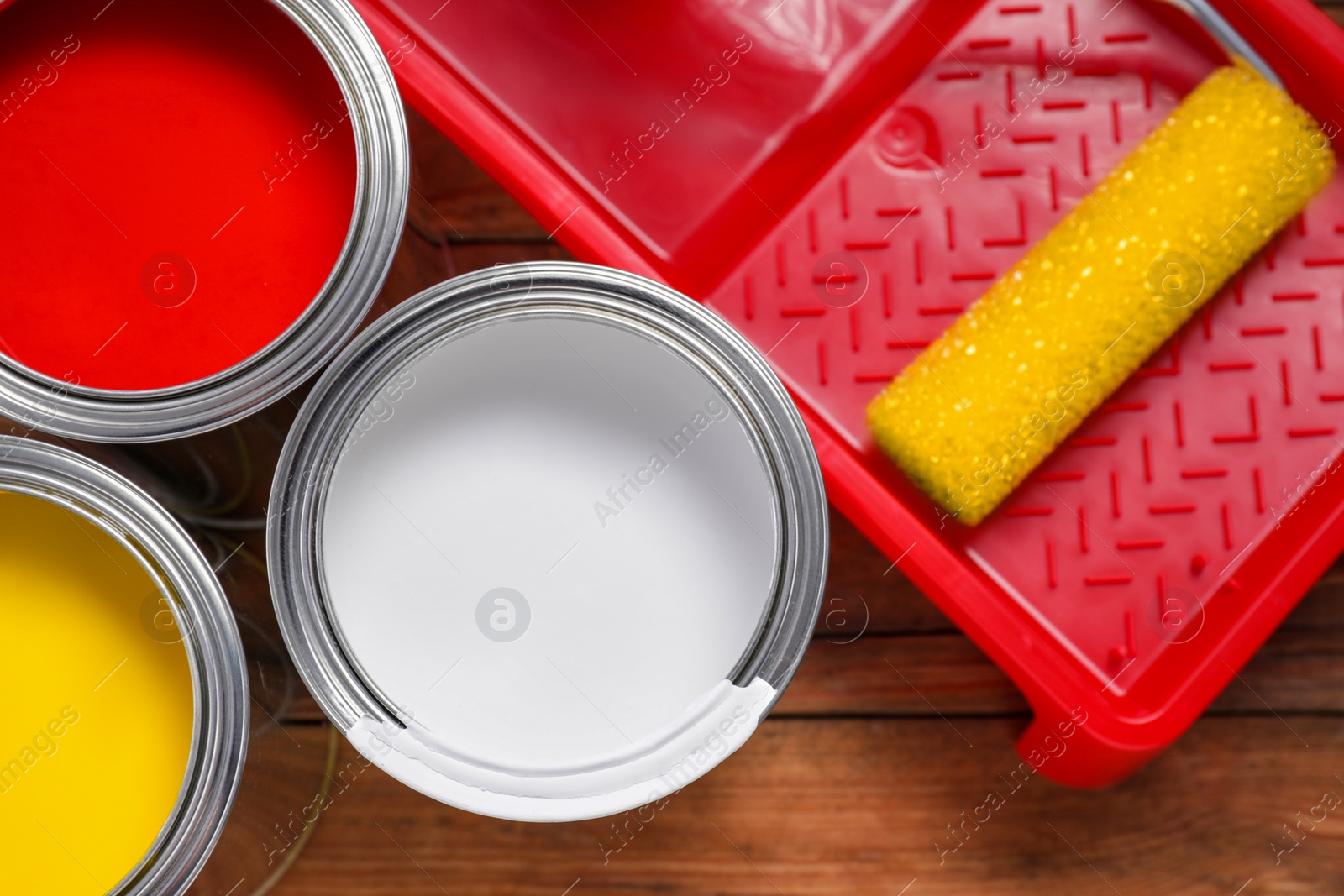 Photo of Cans of paints, roller and tray on wooden table, flat lay