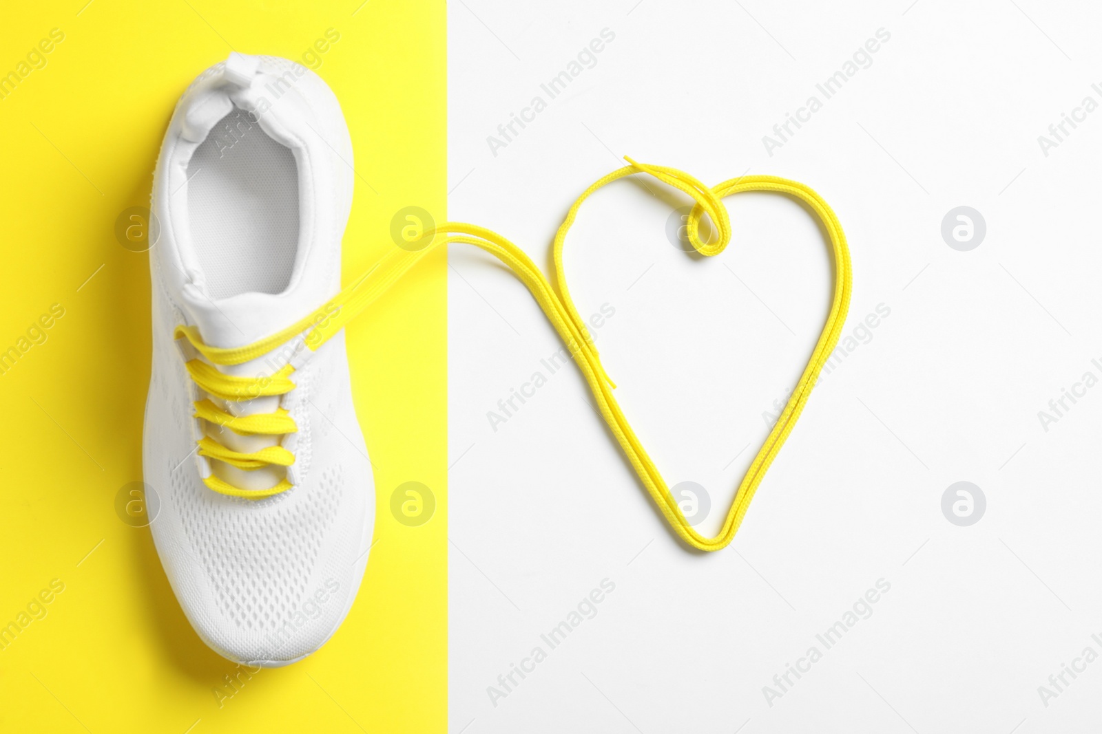 Photo of Stylish sportive shoe and yellow laces in shape of heart on color background, flat lay