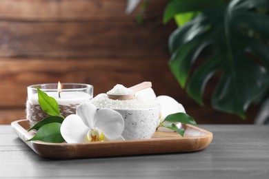 Photo of Natural sea salt in bowl, candle and beautiful orchid flower on wooden table. Space for text