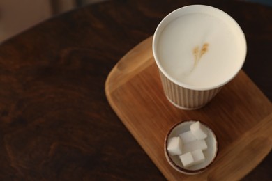 Photo of Delicious coffee in cardboard takeaway cup and bowl of sugar cubes on wooden table, above view. Space for text