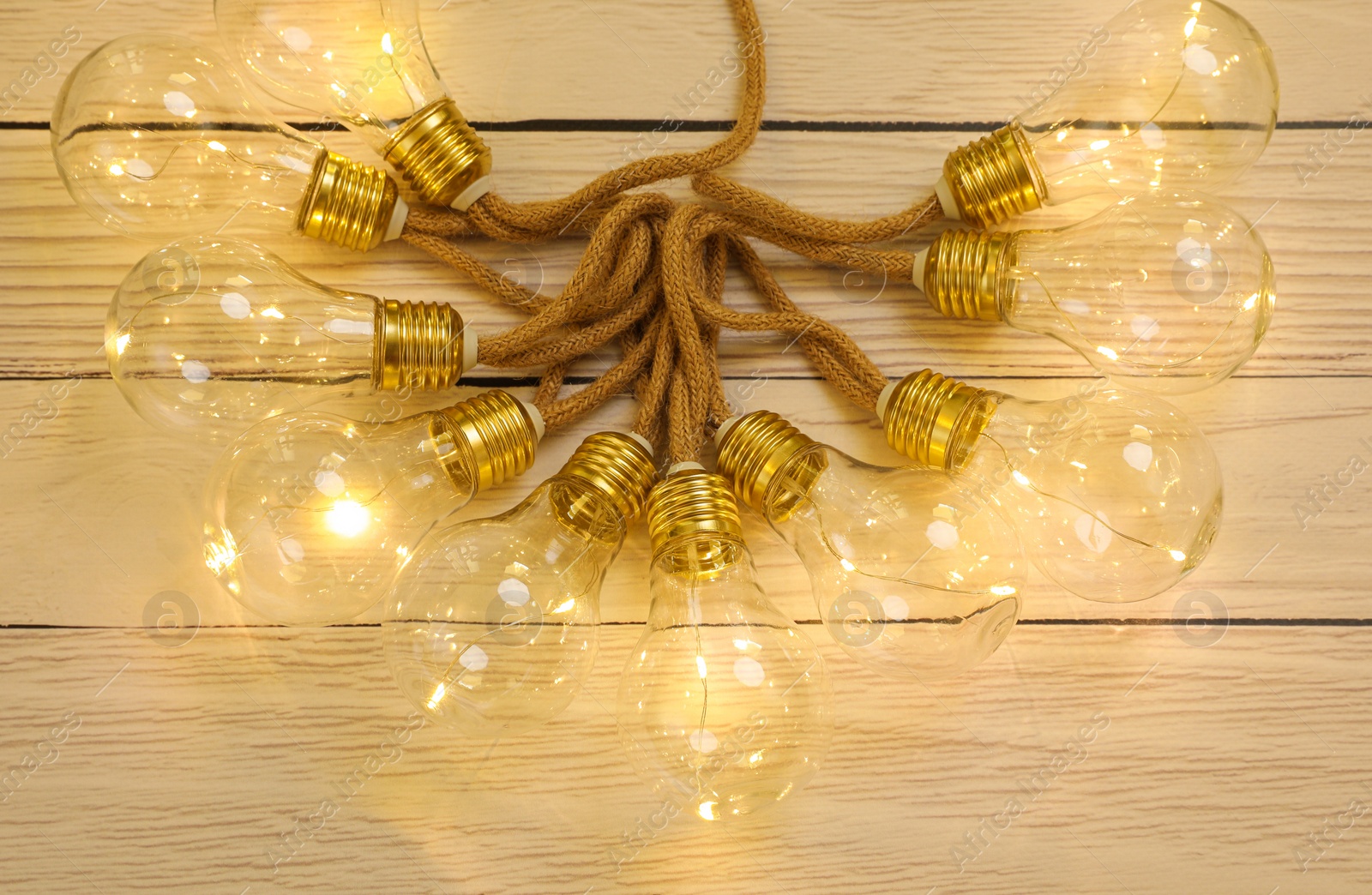 Photo of String lights with lamp bulbs on wooden background, top view