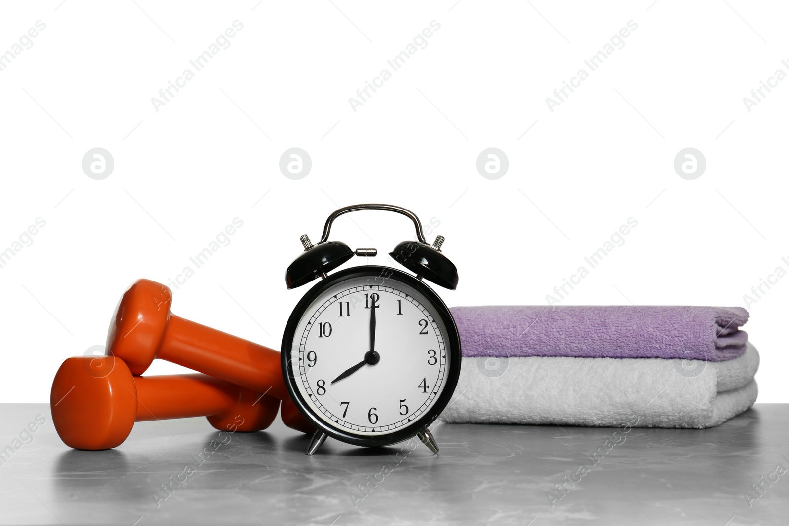 Photo of Alarm clock, towels and dumbbells on marble table against grey background. Morning exercise