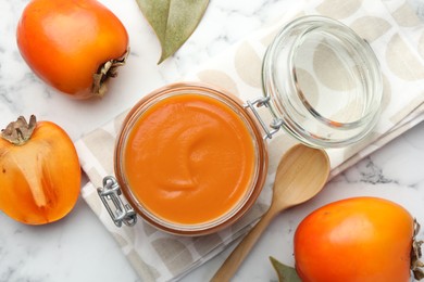 Delicious persimmon jam and fresh fruits on white marble table, flat lay