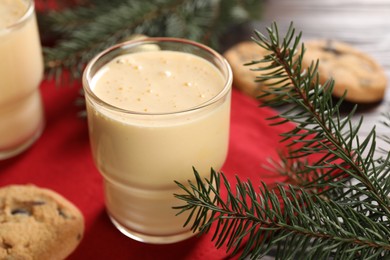 Photo of Tasty eggnog, cookies and fir branches on wooden table, closeup