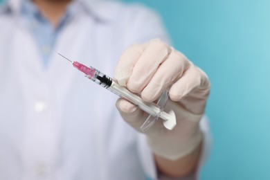 Doctor holding syringe on light blue background, closeup