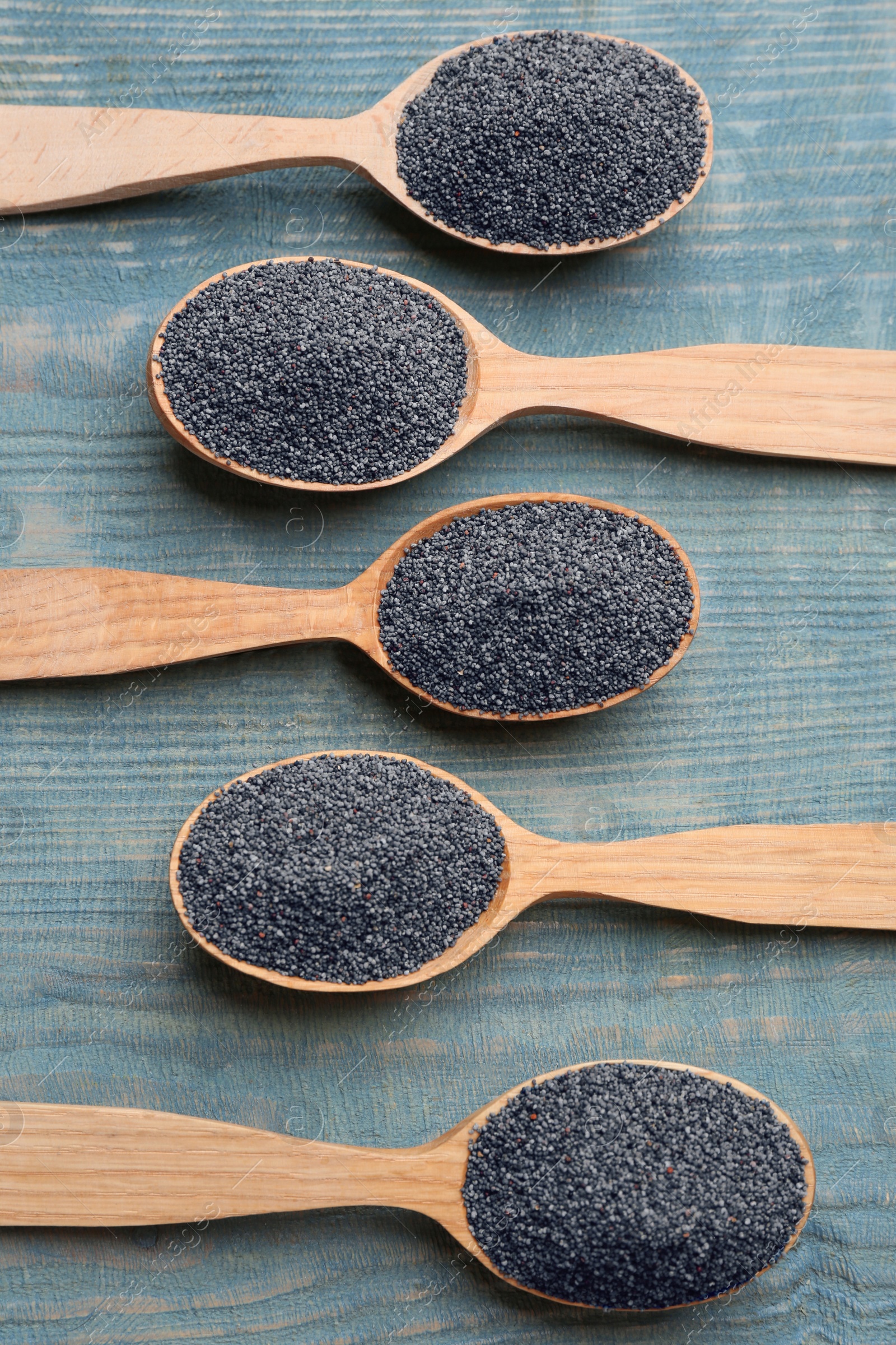 Photo of Poppy seeds in spoons on blue wooden table, flat lay