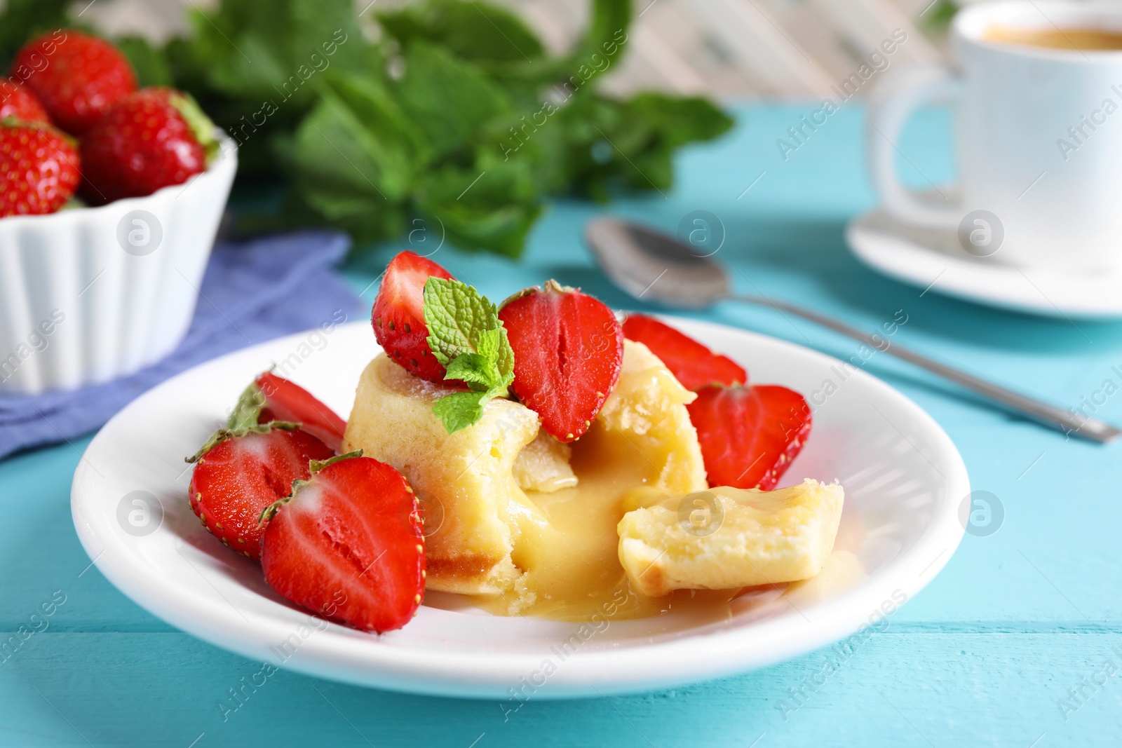 Photo of Tasty vanilla fondant with white chocolate and strawberries on light blue wooden table, closeup