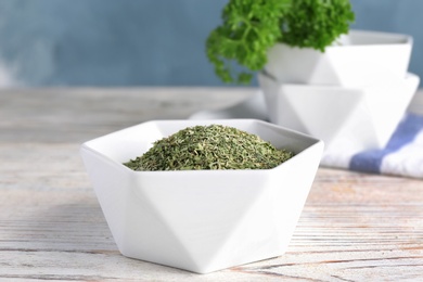 Photo of Bowl with dry parsley on wooden table