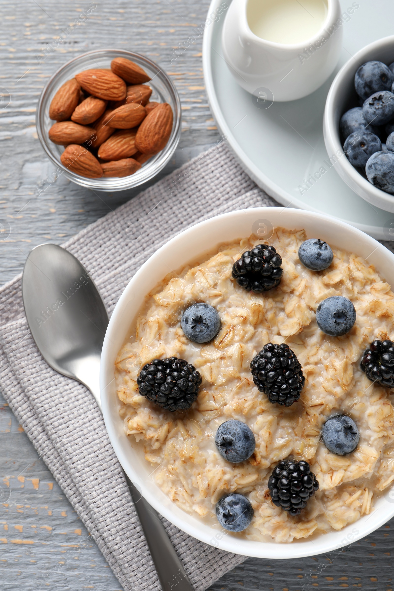 Photo of Tasty oatmeal porridge with blackberries and blueberries served on light grey wooden table, flat lay