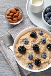 Photo of Tasty oatmeal porridge with blackberries and blueberries served on light grey wooden table, flat lay