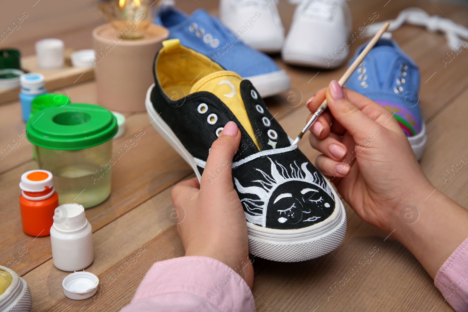 Photo of Woman painting on sneaker at wooden table, closeup. Customized shoes