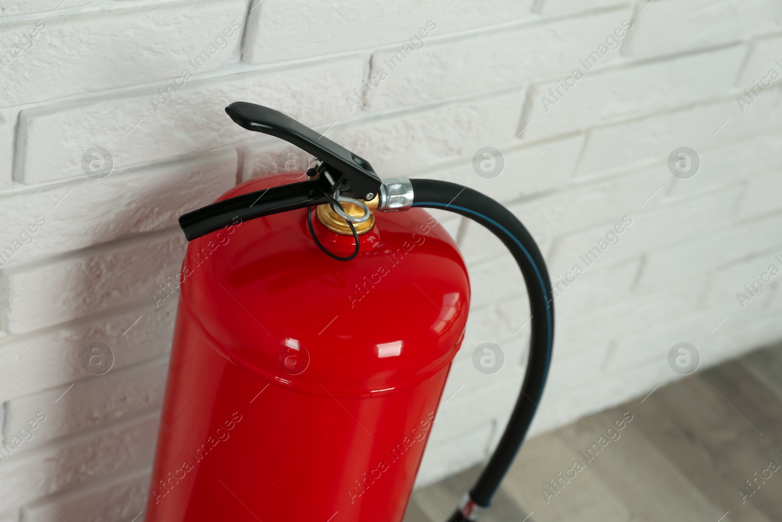 Photo of Fire extinguisher near white brick wall indoors, closeup