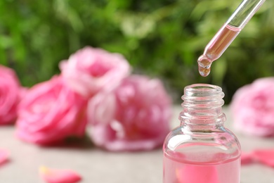 Photo of Dripping rose essential oil into bottle against blurred background. Space for text