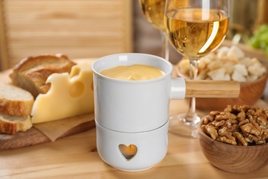 Pot of tasty cheese fondue and products on wooden table