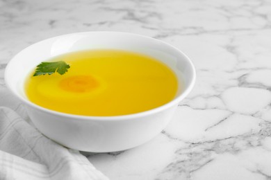 Photo of Delicious bouillon with egg and parsley in bowl on white marble table
