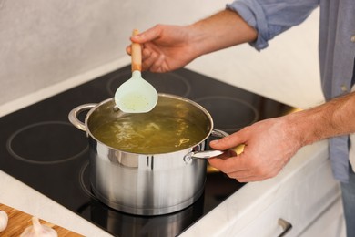 Photo of Man cooking delicious chicken soup in kitchen, closeup