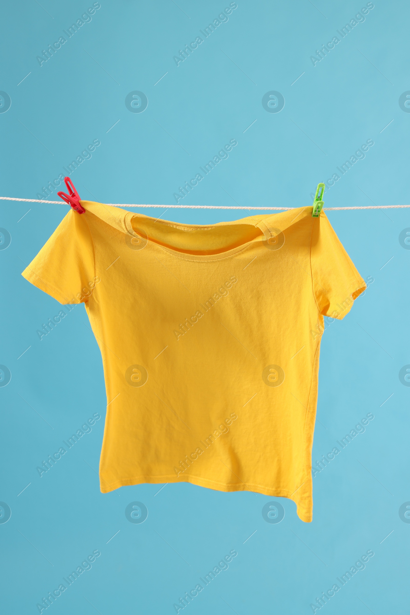 Photo of One yellow t-shirt drying on washing line against light blue background