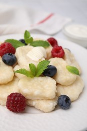 Photo of Tasty lazy dumplings with berries, butter and mint leaves on plate, closeup