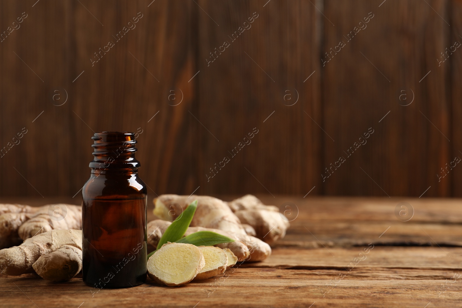 Photo of Glass bottle of essential oil and ginger root on wooden table, space for text