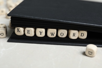 Photo of Beads with word KEYWORD in notebook on light marble table, closeup