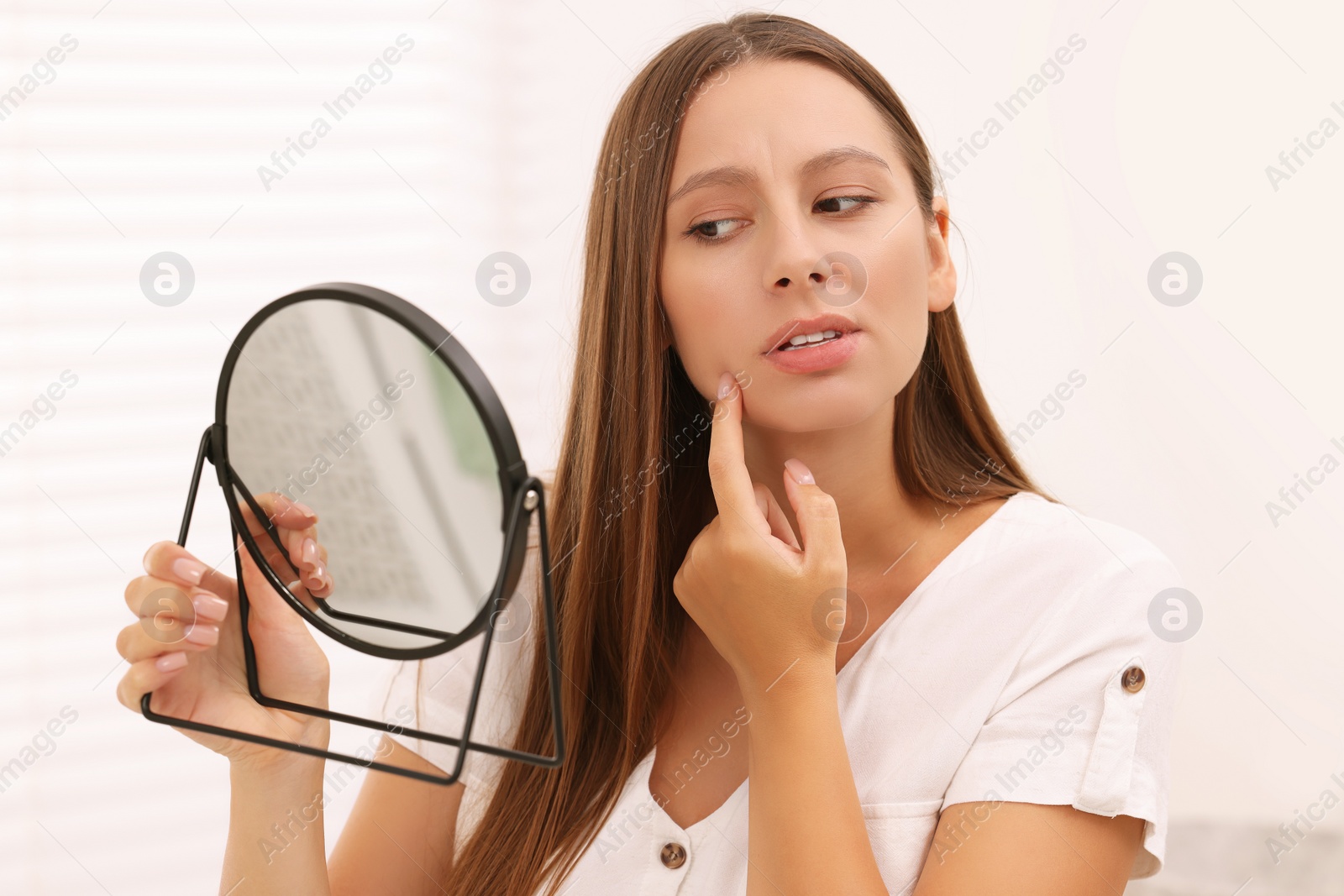 Photo of Woman with skin problem looking at mirror indoors