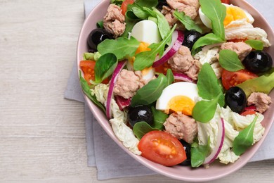 Photo of Bowl of delicious salad with canned tuna and vegetables on white wooden table, top view