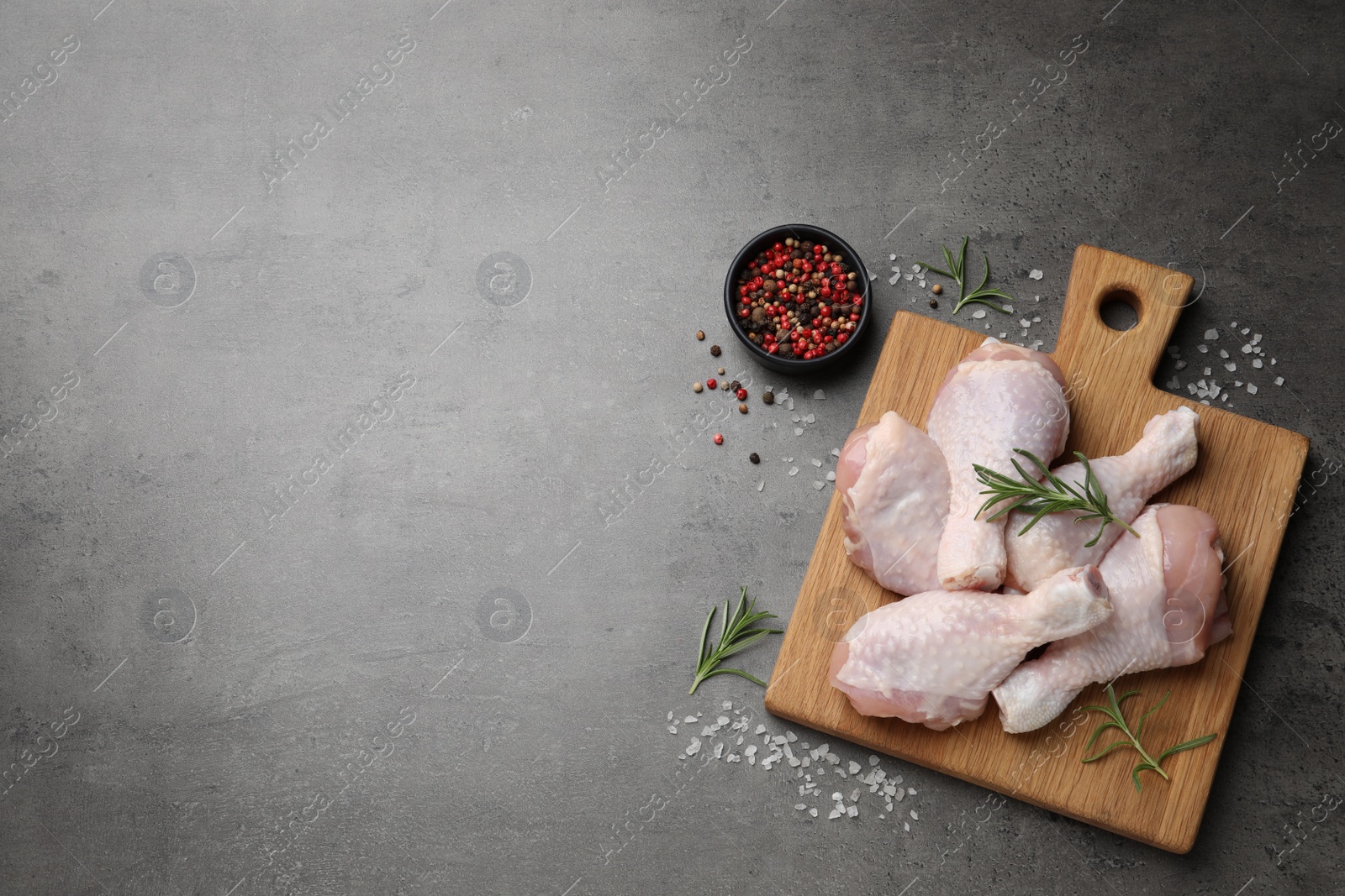 Photo of Raw chicken drumsticks with rosemary and spices on grey table, flat lay. Space for text